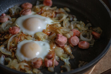Chicken egg fried in a pan with onions and sausages, close-up.