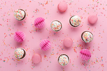 Pink paper decorations, sweet macaroons and cupcakes on pink sprinkles background.