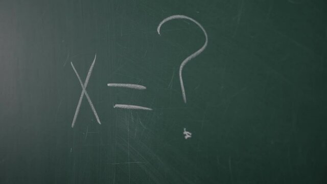 Close-up of a math teacher writes math formulas and problems with chalk on a green blackboard during a lesson in high school.