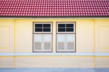 Vintage yellow wall of building with double closed white window and red tiles roof