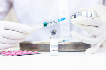 A syringe with a vaccine is held in hands. A vial with a vaccine is on the table