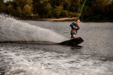 sportive guy holding taut rope and rides down on wave on wakeboard