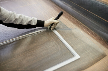 Close-up of a man's hands mounting a mosquito net for PVC Windows in a factory.