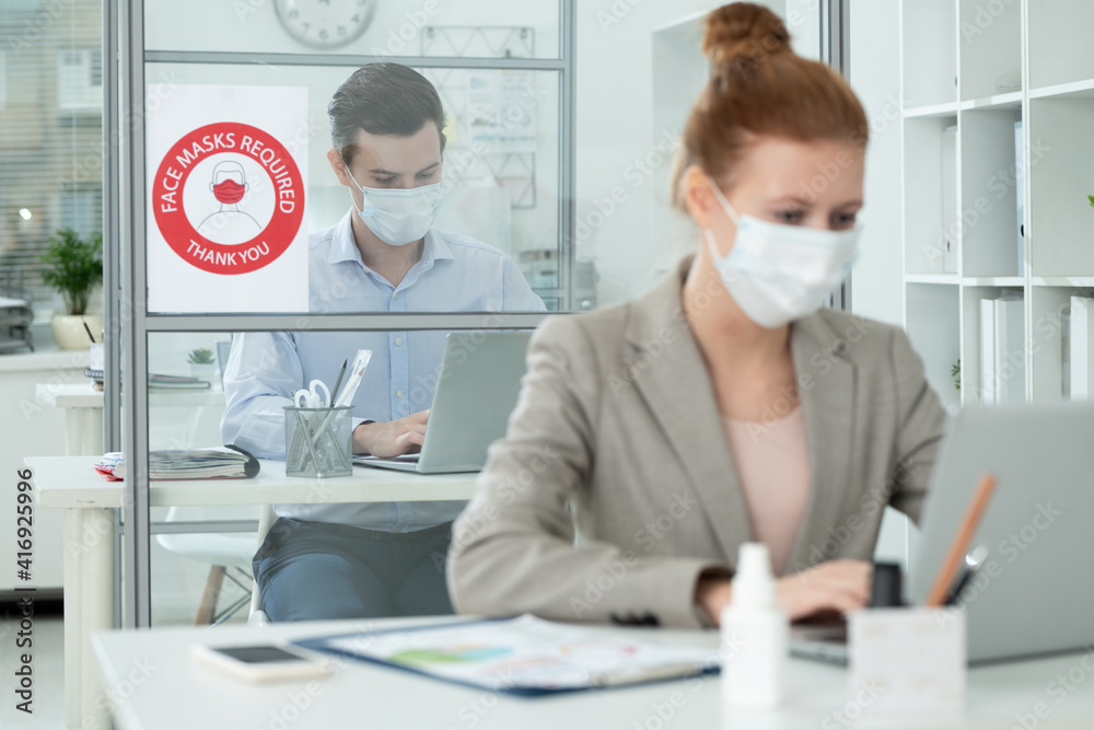 Poster elegant man in protective mask networking in office in front of female colleague