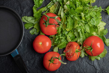 Empty pan, tomatoes and parsley leaves on black background