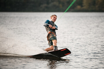 young cheerful guy actively spends his leisure time and balances on wakeboard on water.