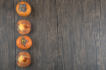 Whole and sliced fuyu persimmon fruits on wooden surface