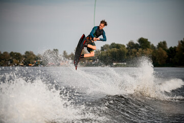 young adult guy skillfully jumps on wakeboard above the splashing river wave