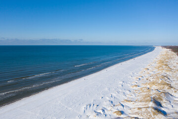 Fototapeta na wymiar Aerial view of snow covered beach and dunes and blue calm sea