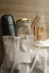 Sustainable kitchen in linen tote bag: thermos bottle, mason jar, wooden spoon and metal straws. Top view.