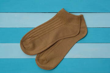 Knitted short socks on a colored wooden background top view. Brown cotton socks. A pair of sports socks.