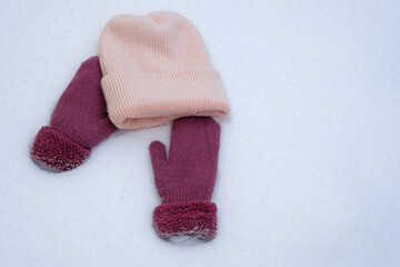Pink knitted hat and mittens on white snow top view. Warm clothes for winter.