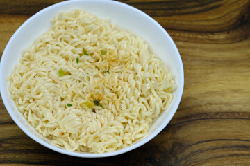 Instant noodles in a white plate top view. Fast food with spices for lunch on a wooden background.