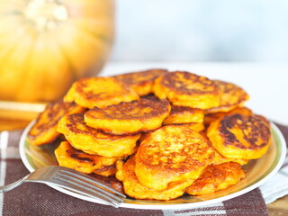 Diet healthy food idea.Fried pumpkin pancakes in a plate on the background of a large orange pumpkin.