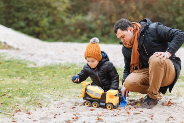 parent and child playing. Father with child playing in the sand with a cement mixer. Autumn colors. Children play with me outside. Father and son in autumn or spring 