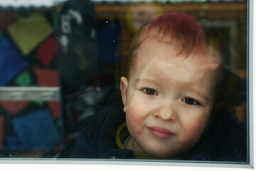 cute toddler baby boy close up portrait with flat nose agains the window with reflection