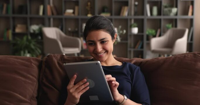 Relaxed young indian woman using modern digital computer tablet, enjoying web surfing information, shopping in internet store, communicating distantly with friends or working in software app.