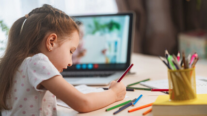 little girl, a preschooler, uses a laptop to study at home. the child smiles happily and receives knowledge remotely. digital concept of e-learning. Distance e-learning. View from over the shoulder
