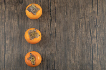 Three ripe persimmon fruits placed on wooden surface