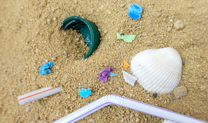 Fototapeta na wymiar Close-up On Plastic Trash On The Beach. Straws, a Bottle Cap, And Plastic Pieces. on Recyclable Materials. Selective Focus With Shallow Depth Of Field. Selective Focus On Garbage On The Beach.