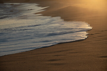 Wave reaching the beach at sunset.