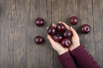 Woman hands holding healthy purple plums on wooden table