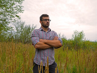 A young man in a bright shirt and glasses stands in nature in the green grass