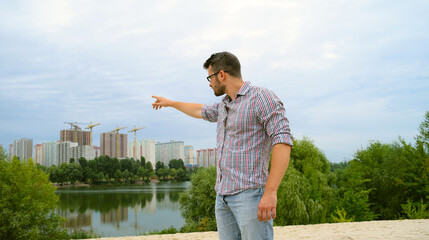 Young man in a shirt shows with his hand to the city in the distance