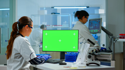 Medical research scientist working on pc with green screen mock up template in applied science laboratory. Engineers conducting experiments in background, examining vaccine evolution using high tech