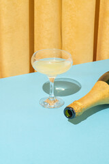Minimal retro vintage scene with champagne glass and bottle on pastel blue table against yellow...