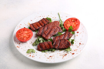 Slices of roast meat with spices, herbs and tomatoes on a white plate on a white table. Restaurant menu, background image, copy space, horizontal. Fried beef