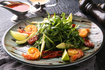 Salad with arugula and shrimp, prawns, avocado, lime and sun-dried tomatoes on a gray plate on a black table. Restaurant menu, background image, copy space, horizontal