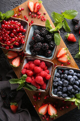 Fresh berries. Red currants, blackberries, blueberries and raspberries in bowls on a large wooden board with mint leaves, strawberries and pomegranate seeds. Background image, top view, vertical