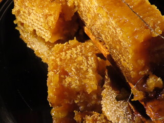 Organic honey from various flowers in honeycomb with wax caps on being taken out of wooden frame. Close up, selective focus