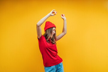A modernly dressed girl is emotionally dancing. Yellow background, studio photo. Place for text