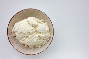 Close-up of freshly made white soft cottage cheese in bowl on white background. Homemade ricotta on table. Top view	
