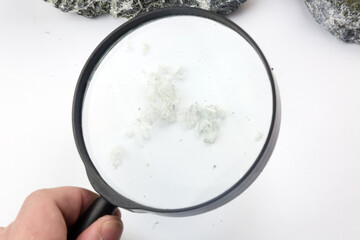 Hand with magnifying glass examines asbestos fibers in stone