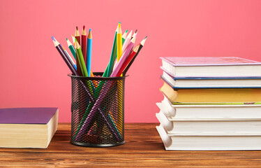 Fototapeta premium A stack of books, colored pencils on a pink background.