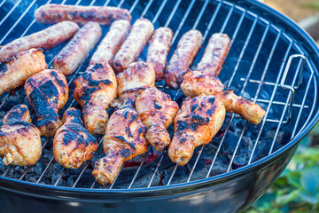 Burnt, charred chicken. Process cooking chicken drumstick and sausages on barbecue grill outdoors. Picnic, eating outdoors. Metal barbecue grill (brazier).