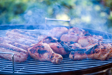 Burnt, charred chicken. Process cooking chicken drumstick and sausages on barbecue grill outdoors. Picnic, eating outdoors. Metal barbecue grill (brazier).