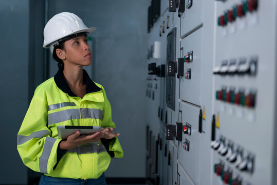  Female Industrial Engineers in Hard Hats checking job in electrical control room.