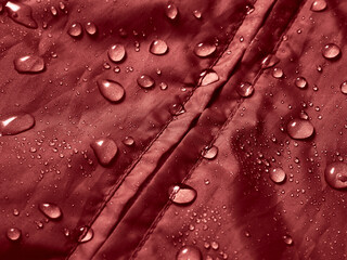Water drops on waterproof membrane fabric. Detail view of texture of red waterproof cloth.