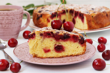 Homemade cut pie with cherries is located on a plate on a white background with cup of coffee.
