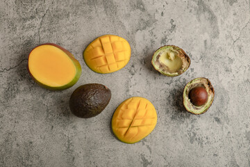 Sliced tropical fruit mango and broken avocado on marble surface