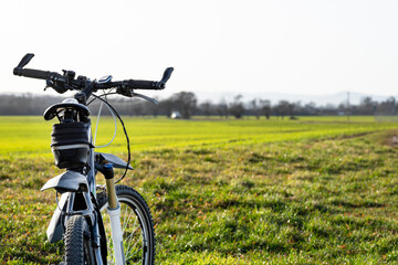 A bicycle handlebar seen from the first person perspective. Visible bicycle frame and bicycle accessories on the handlebar and the field in the background.
