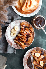 Sweet breakfast. Thin pancakes with caramel, chocolate and banana. Dark background. Top view.