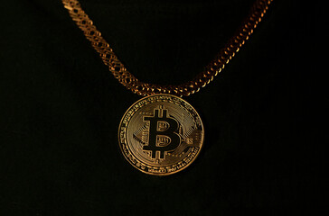 Bitcoin coin hanging on golden chain on black background