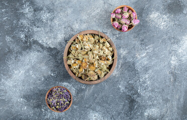 Three bowls of dried flower tea on marble background