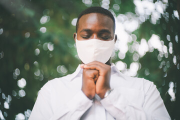 African man praying for god with wearing face mask in the green nature