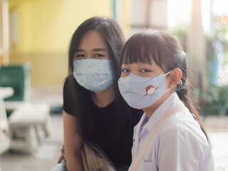 Asian child girl and her mother wearing face mask in school